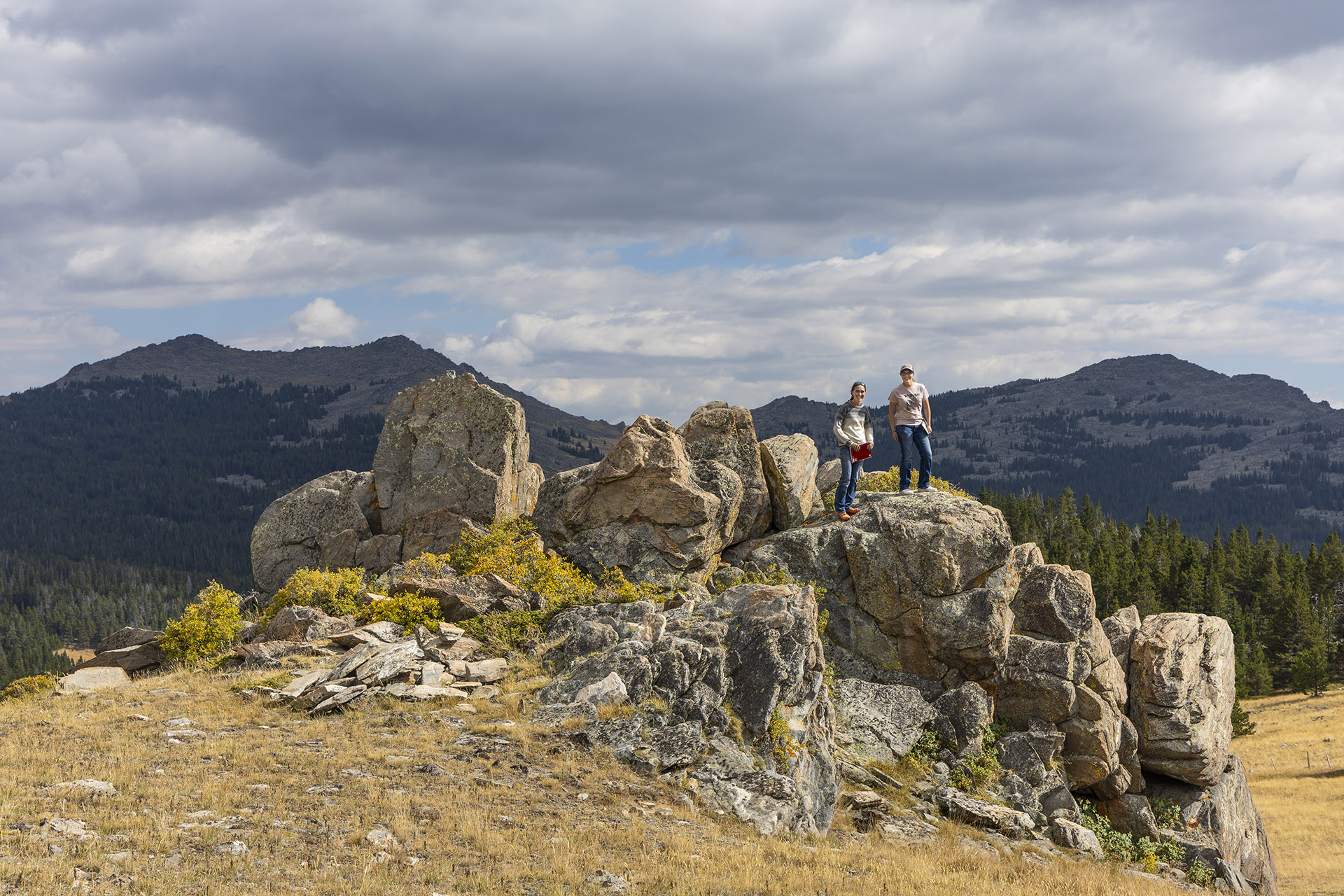 Sheridan College students on a filed trip in the Bighorn Mountains Two Sheridan College students standing on a rocky outcrop with a view of peaks behind them, while on a field trip in the Bighorn Mountains