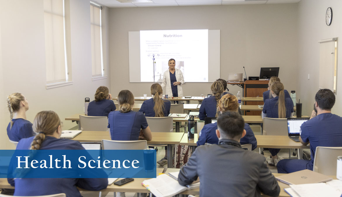 Health Science Classroom full of nursing students as instructor stands in front of projection at the head of the classroom.